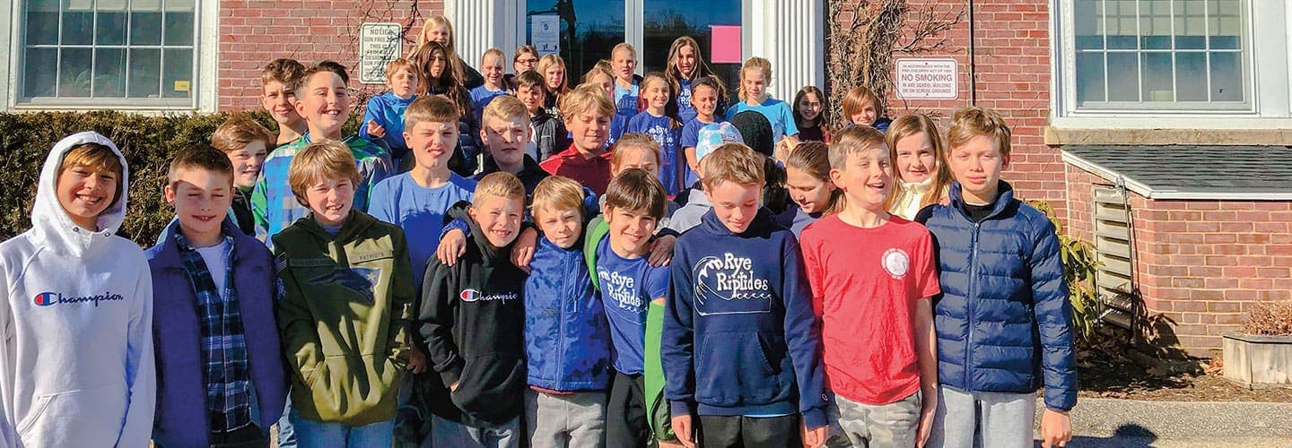 A group of students smile outside their school